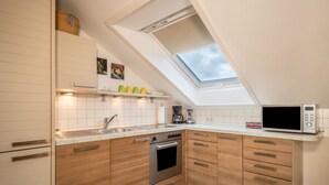 Eine Küche mit Holzausstattung, einem Edelstahlbackofen, einer Mikrowelle und einem Dachfenster.