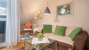 Ein modernes Wohnzimmer mit einem Glastisch, einem braunen Sofa mit grünen Kissen, einem Holzstuhl und einer Stehlampe.