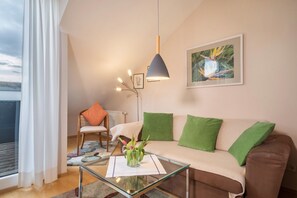 Un salon moderne avec une table basse en verre, un canapé marron agrémenté de coussins verts, une chaise en bois et un lampadaire.
