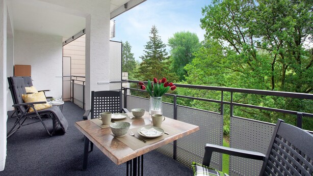 Un balcone con tavolo apparecchiato per mangiare, sedie e un vaso con tulipani rossi.