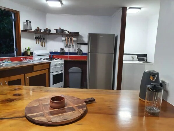 A kitchen with a wooden table, a gas stove, an oven, a refrigerator, and a coffee maker. - Treeverb Beach House : Hexagonal Beach house in the Daintree (Cow Bay)
