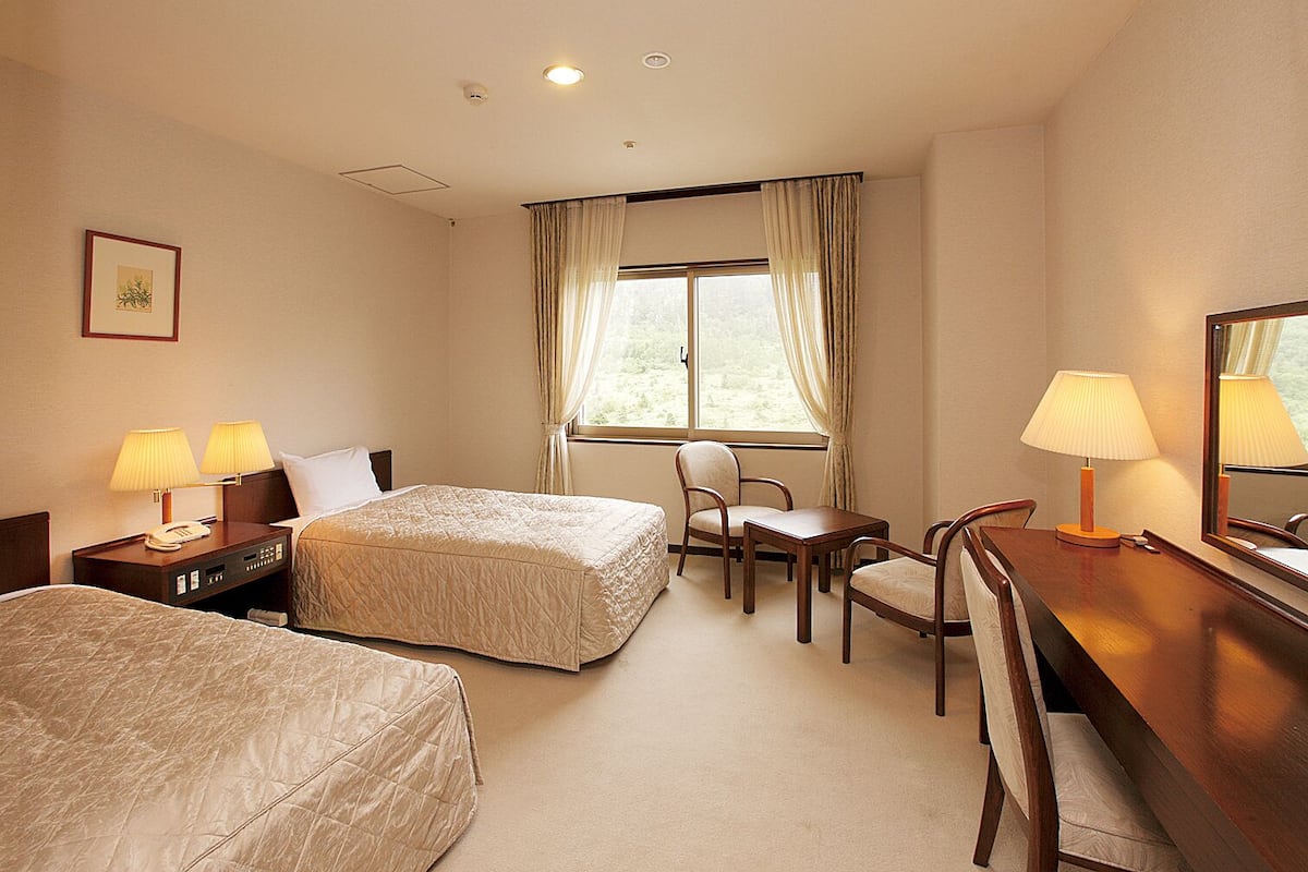 A hotel room with two beds, a desk, a chair, and a window with curtains.