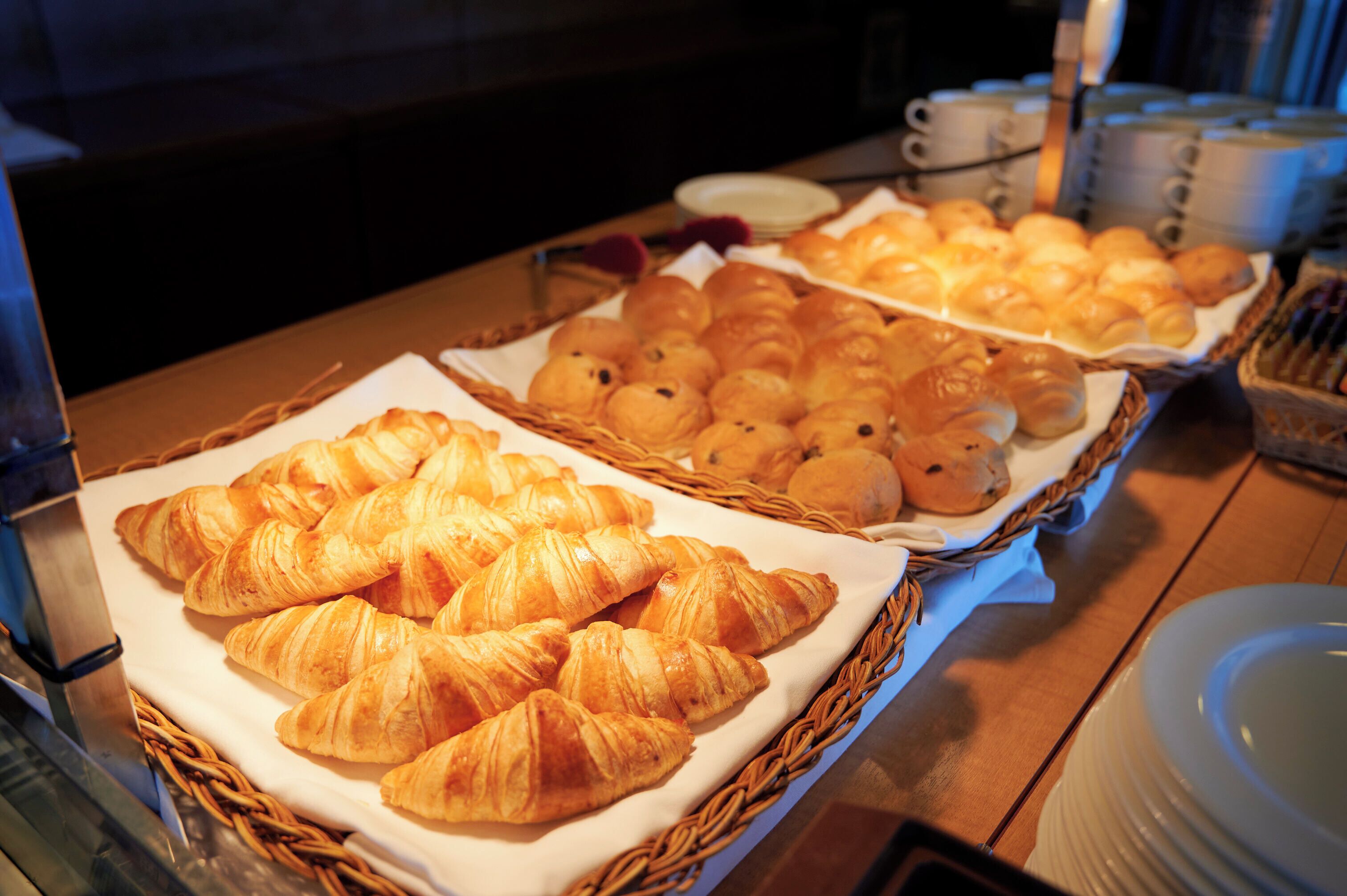Una mesa de buffet con diversos productos horneados, incluyendo cruasanes y otras reposterías, dispuestas en cestas.