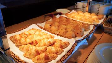 Una mesa de buffet con diversos productos horneados, incluyendo cruasanes y otras reposterías, dispuestas en cestas.
