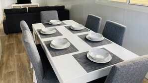 A modern dining area with a white table set for six, grey upholstered chairs, and a grey placemat under each plate. - Modern Cottage amongst nature (Castlereagh)