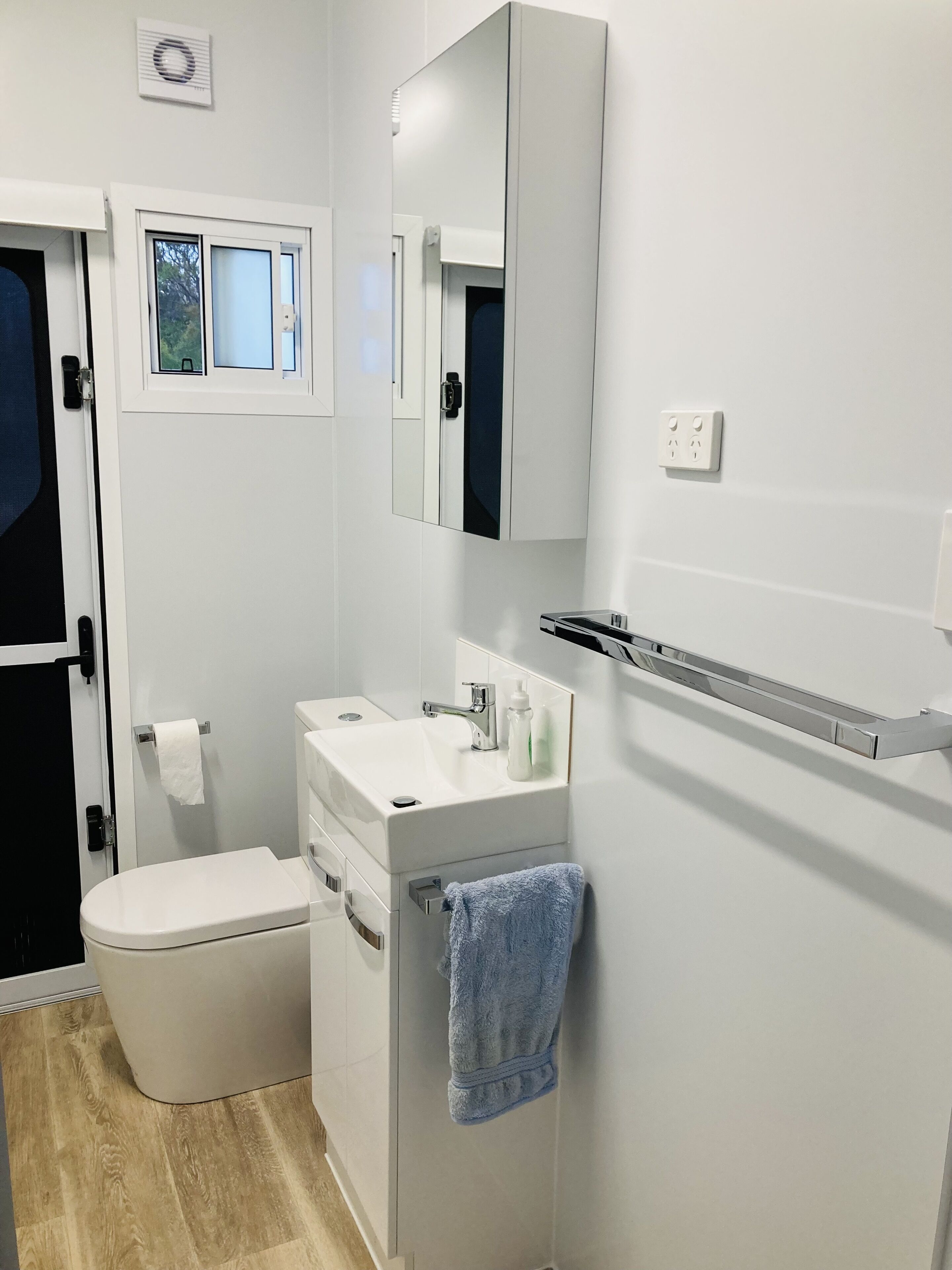 A modern bathroom with a white toilet, a sink with a mirror above it, and a towel hanging on the wall.