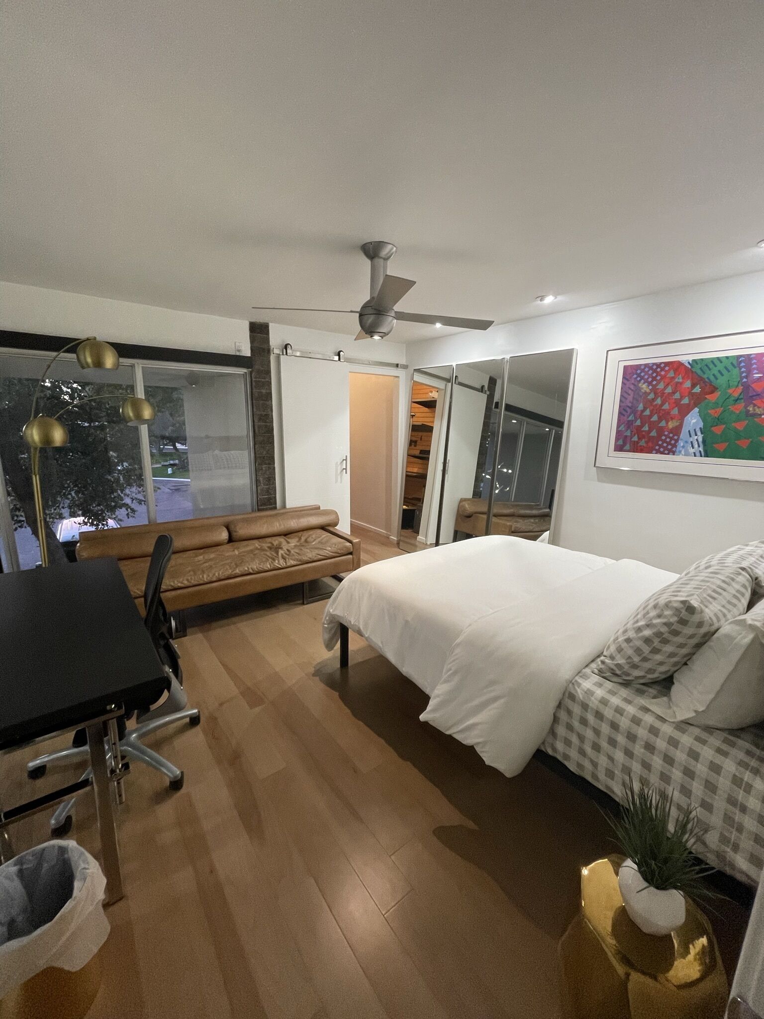 Une chambre moderne comprenant un lit, un bureau, une chaise, un ventilateur de plafond et une grande fenêtre.