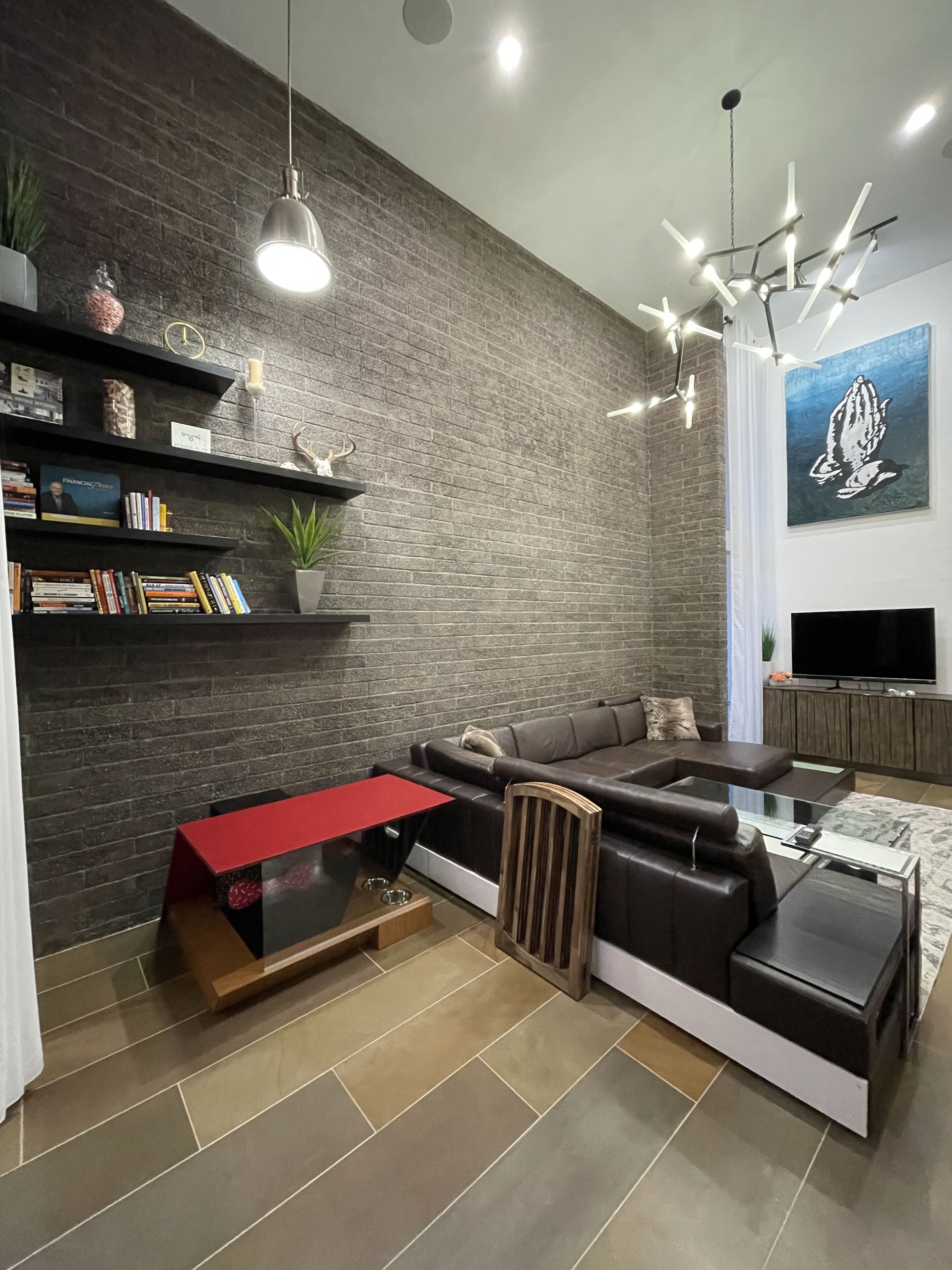 Un salon moderne avec un canapé d’angle, une table basse rouge et un mur en briques.