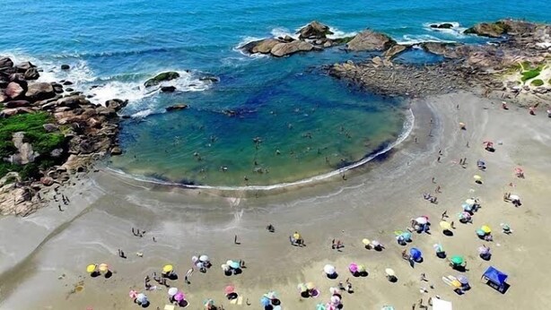 A beach with clear waters, rocky formations, and people sunbathing. - Casa de Praia 80 Metros do mar (Itanhaém)