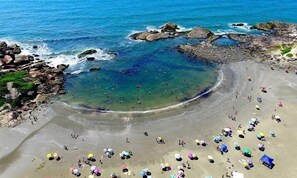 Een strand met helder water, rotsformaties en mensen die aan het zonnebaden zijn.