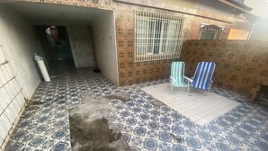 A tiled patio with two striped chairs, a metal gate, and a tiled wall with a window. - Casa de Praia 80 Metros do mar (Itanhaém)