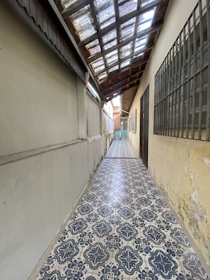 A narrow corridor with patterned tiled flooring, metal bars on windows, and a sloped ceiling.
