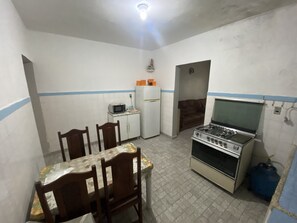A compact kitchen with a gas stove, microwave, refrigerator, and a dining table with chairs.