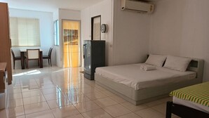 A hotel room with a bed, a desk, a chair, a refrigerator, and an air conditioning unit. - Grandview Condominia (Bangkok)