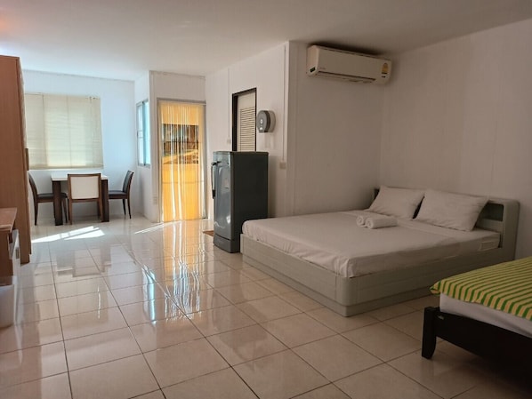 A hotel room with a bed, a desk, a chair, a refrigerator, and an air conditioning unit.