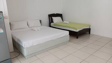 A bedroom with a bed, a smaller bed, and a refrigerator.