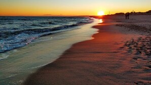 Escena de playa con atardecer, olas y huellas en la arena.