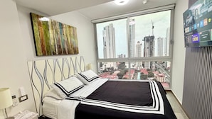 Habitación de hotel moderna con una cama grande, vistas a la ciudad y un televisor con películas disponibles.