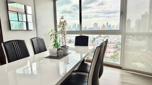 Un salón de conferencias con una amplia mesa, cuatro sillas, una planta en maceta y vistas de la ciudad a través de grandes ventanales.