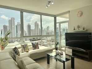 Relax in this stylish living room with a sofa set, flat-screen TV, and city skyline view.