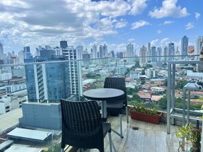 Enjoy breathtaking city views from this rooftop terrace with a table and two chairs, surrounded by lush greenery.