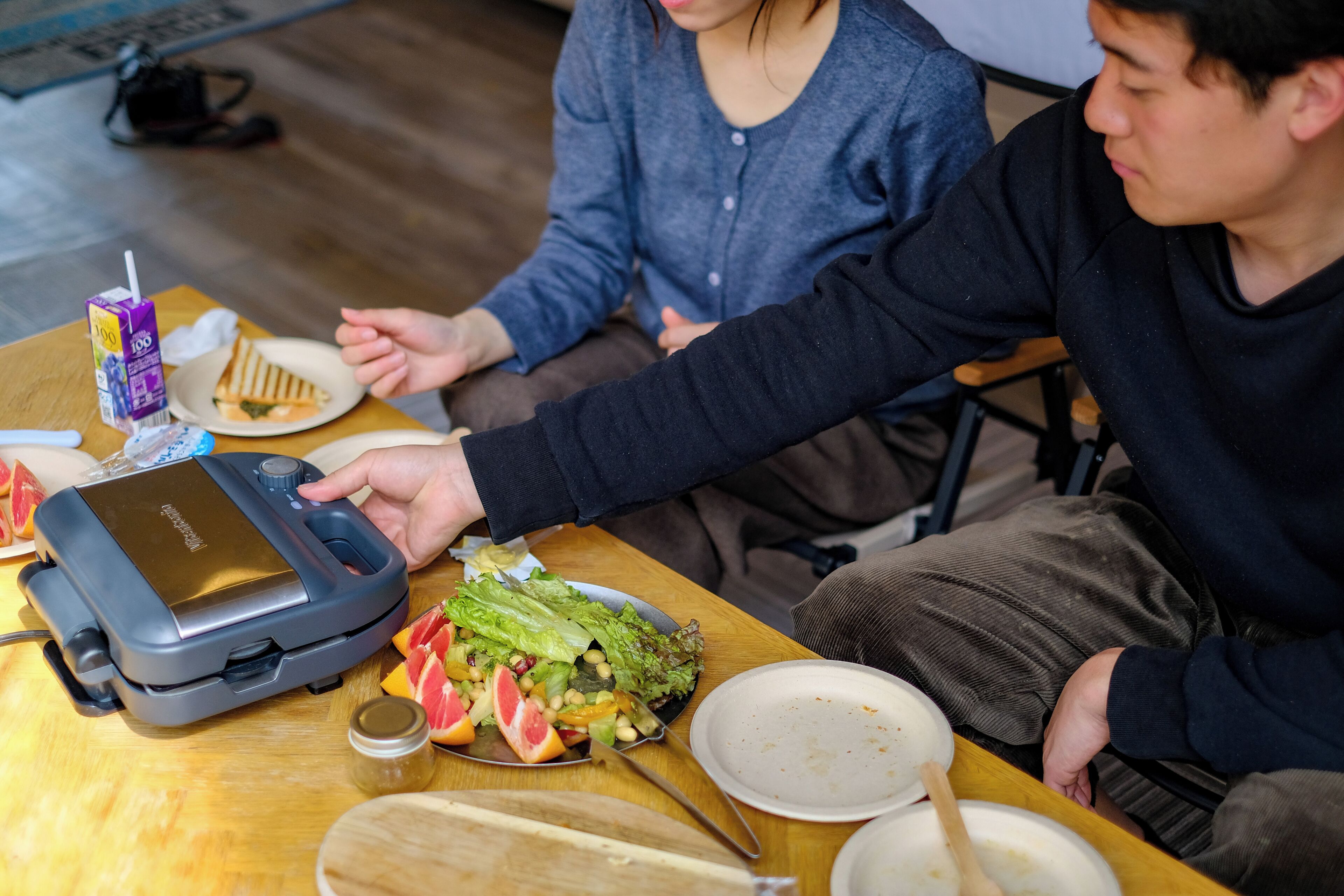 A dining table with a portable food warmer, a plate of food, and a juice carton.