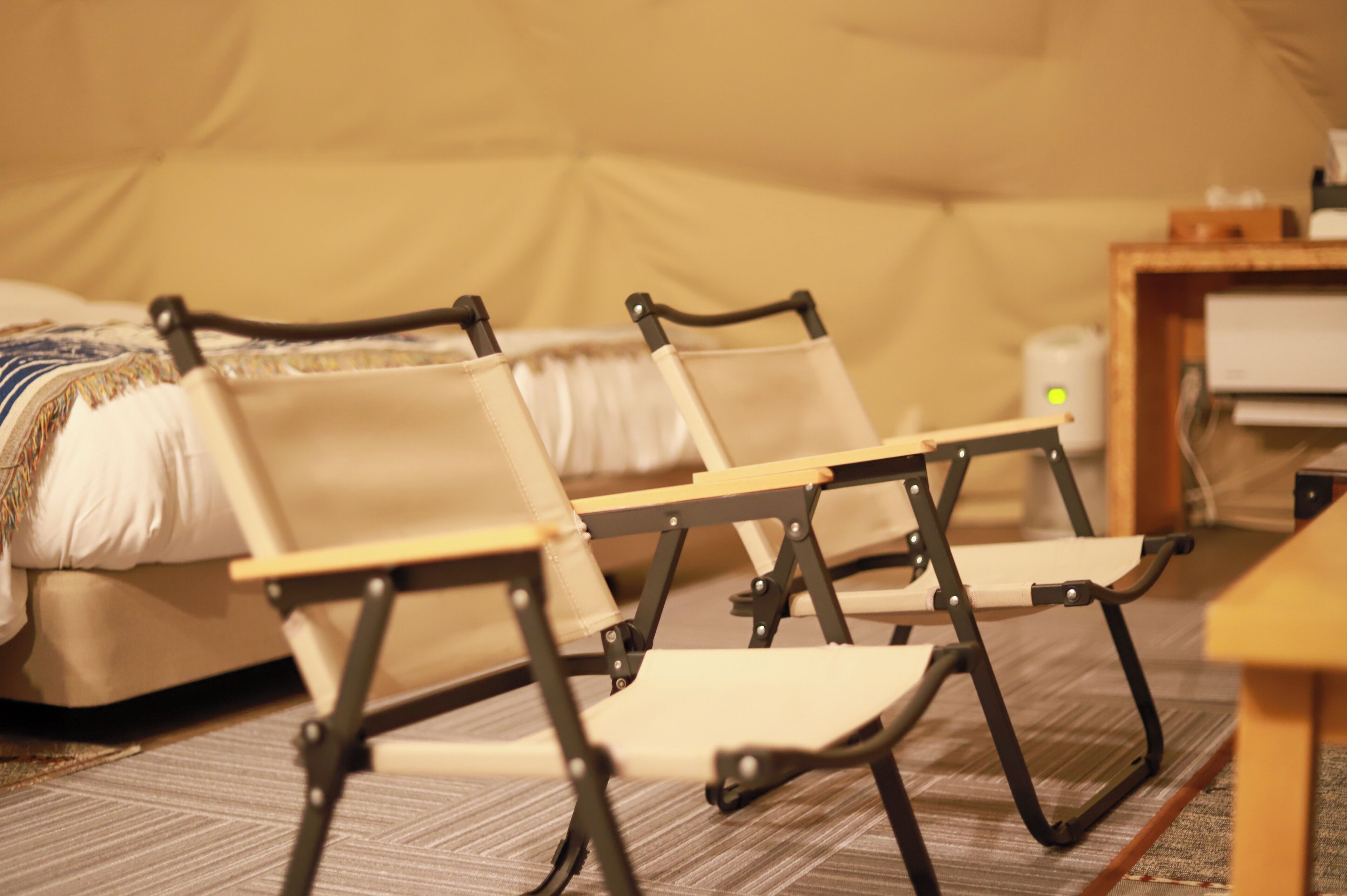 Une pièce comprenant un lit, deux chaises pliantes, une petite table et une lampe.