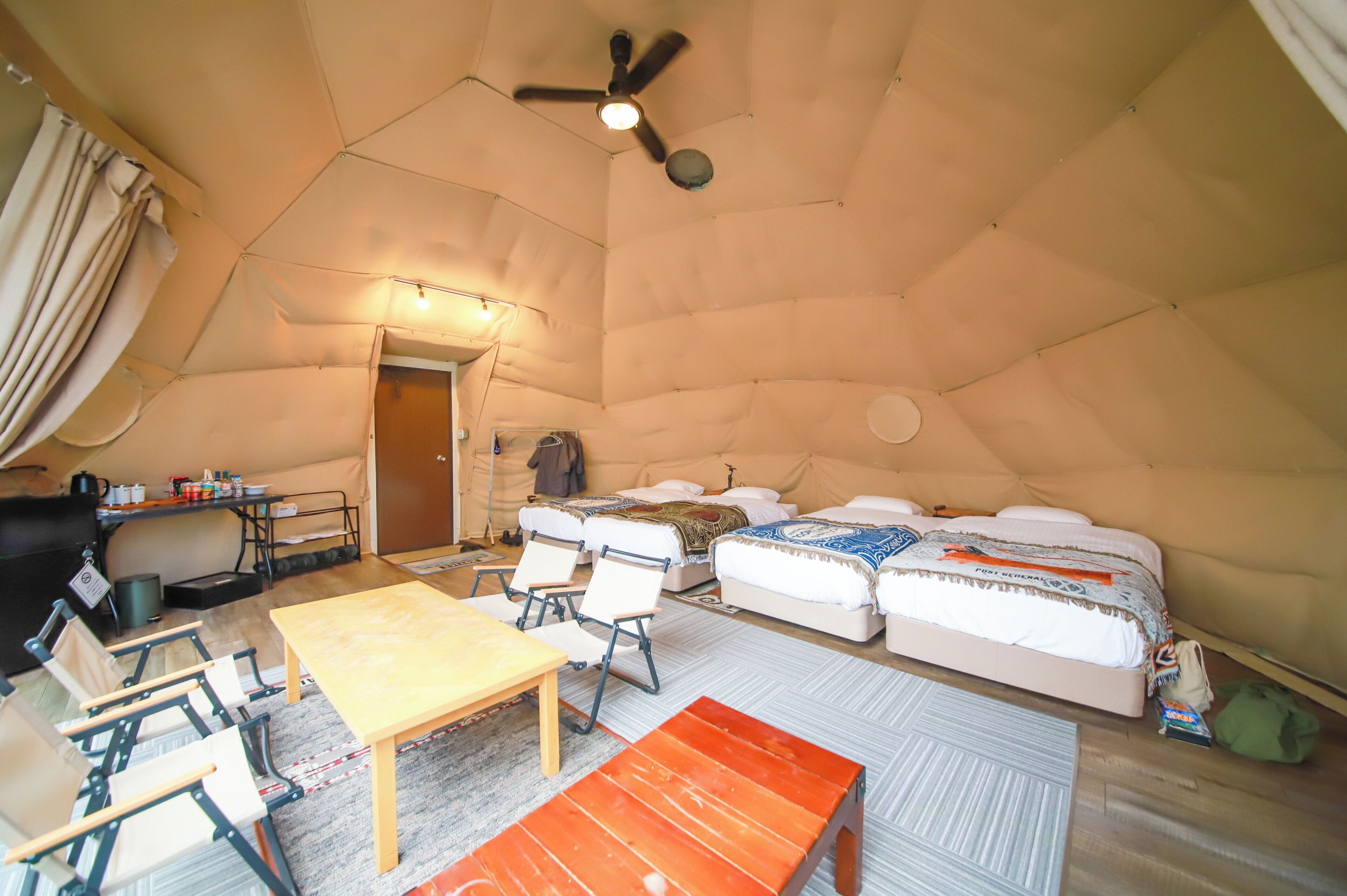 Interno di una tenda con un letto, un tavolo, sedie e una ventola a soffitto.