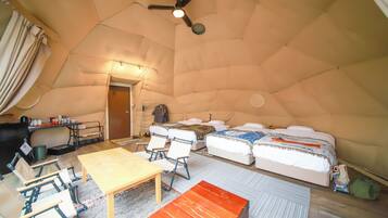 Interno di una tenda con un letto, un tavolo, sedie e una ventola a soffitto.