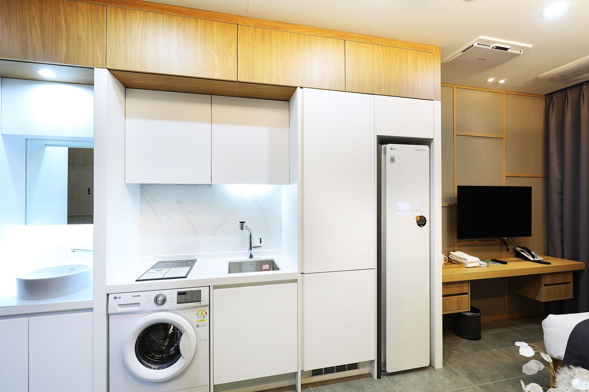 A compact kitchen with a washing machine, a refrigerator, and a flat-screen TV.