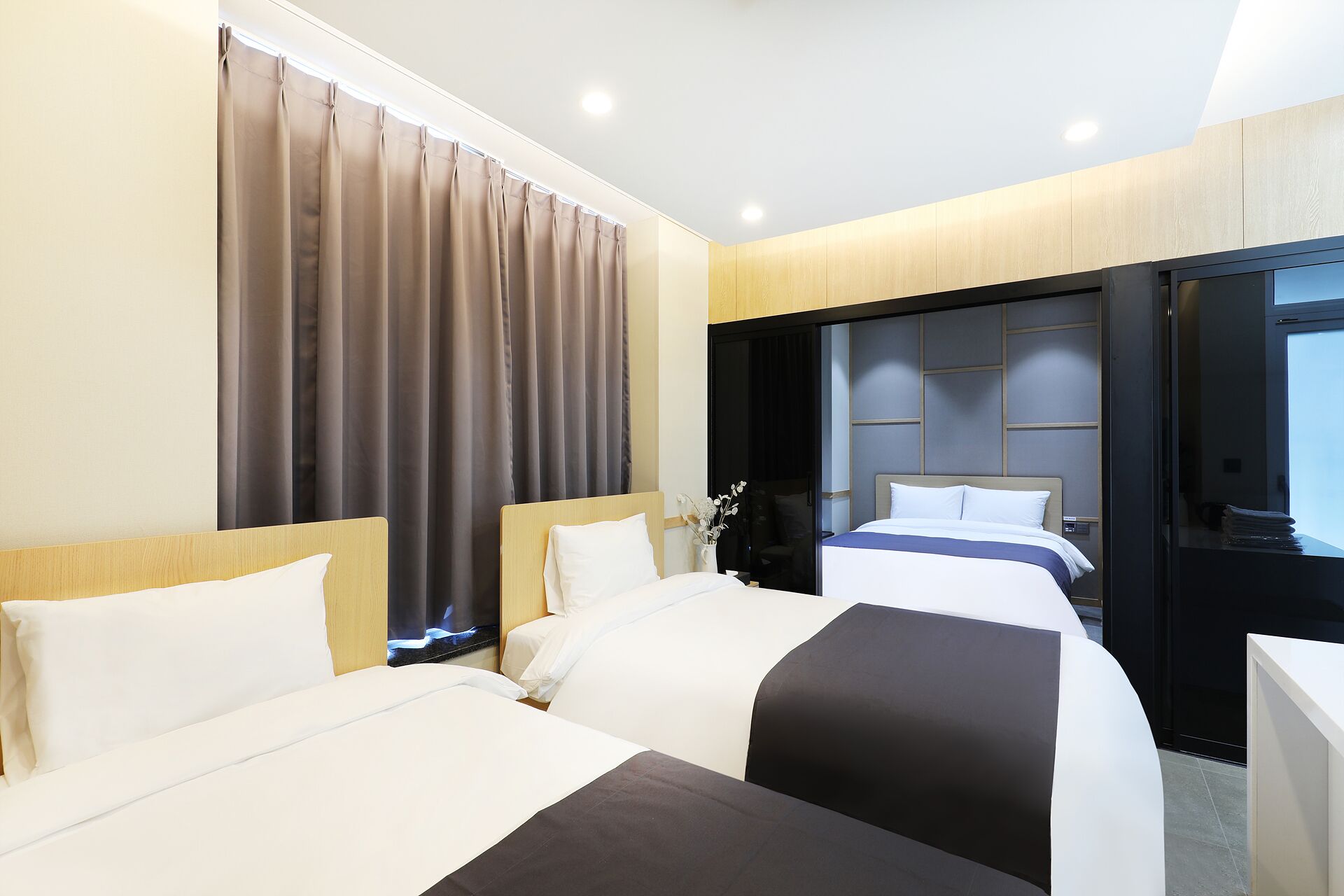 Ein Hotelzimmer mit zwei Betten, einem großen Fenster mit Vorhängen, einem modernen Kopfteil und einem Schreibtisch mit Stuhl.