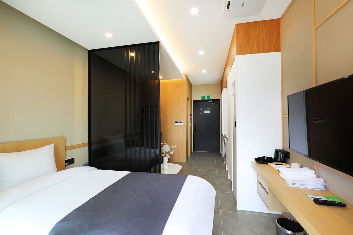 Hotelkamer met een bed, bureau, televisie en een deur met een nooduitgangbord.