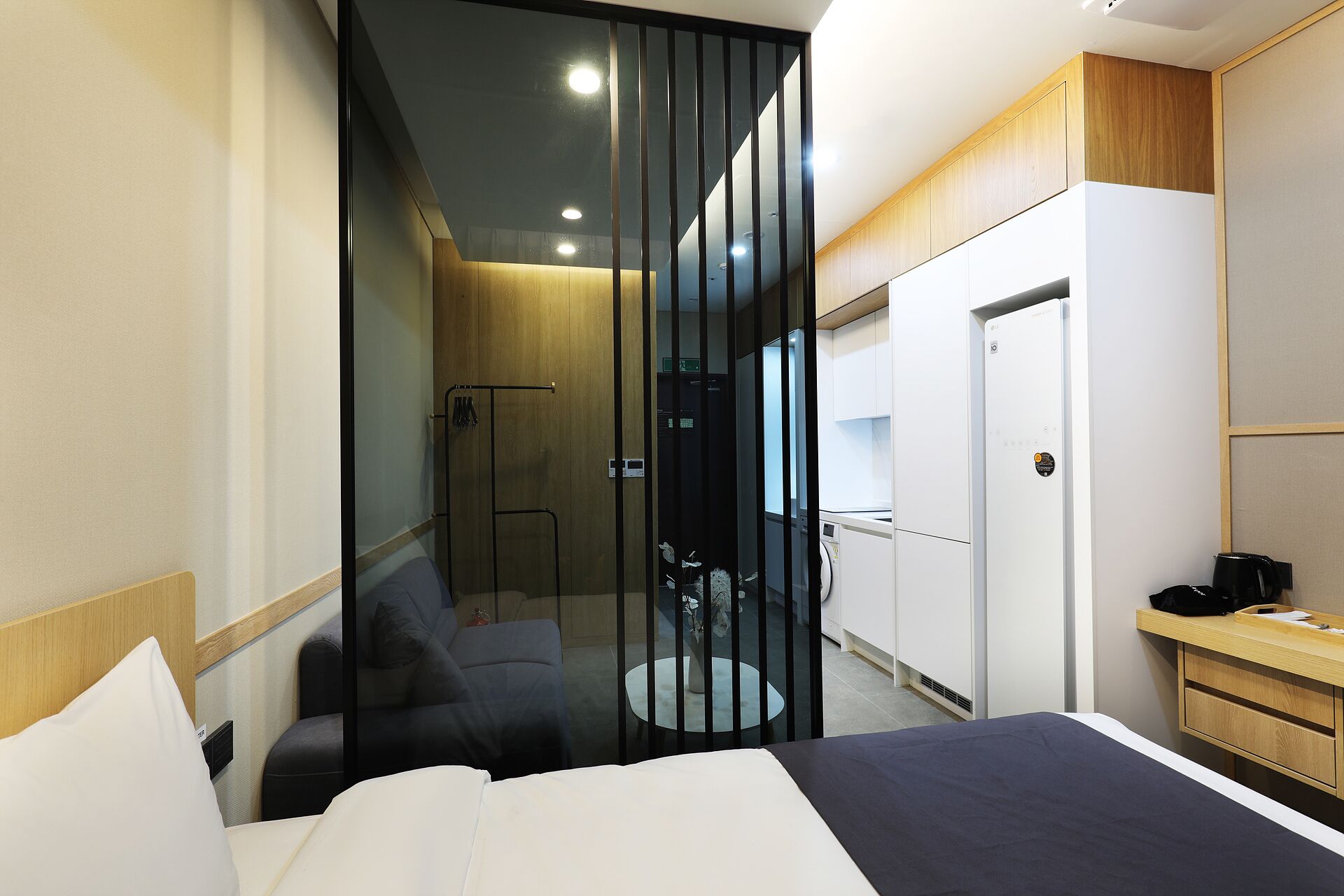 Una habitación de hotel moderna con cama, una zona de estar con sofá y una mesita, armario y zona de ducha.