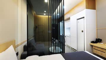 Una habitación de hotel moderna con cama, una zona de estar con sofá y una mesita, armario y zona de ducha.