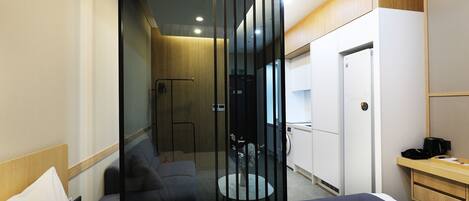 Una habitación de hotel moderna con cama, una zona de estar con sofá y una mesita, armario y zona de ducha.