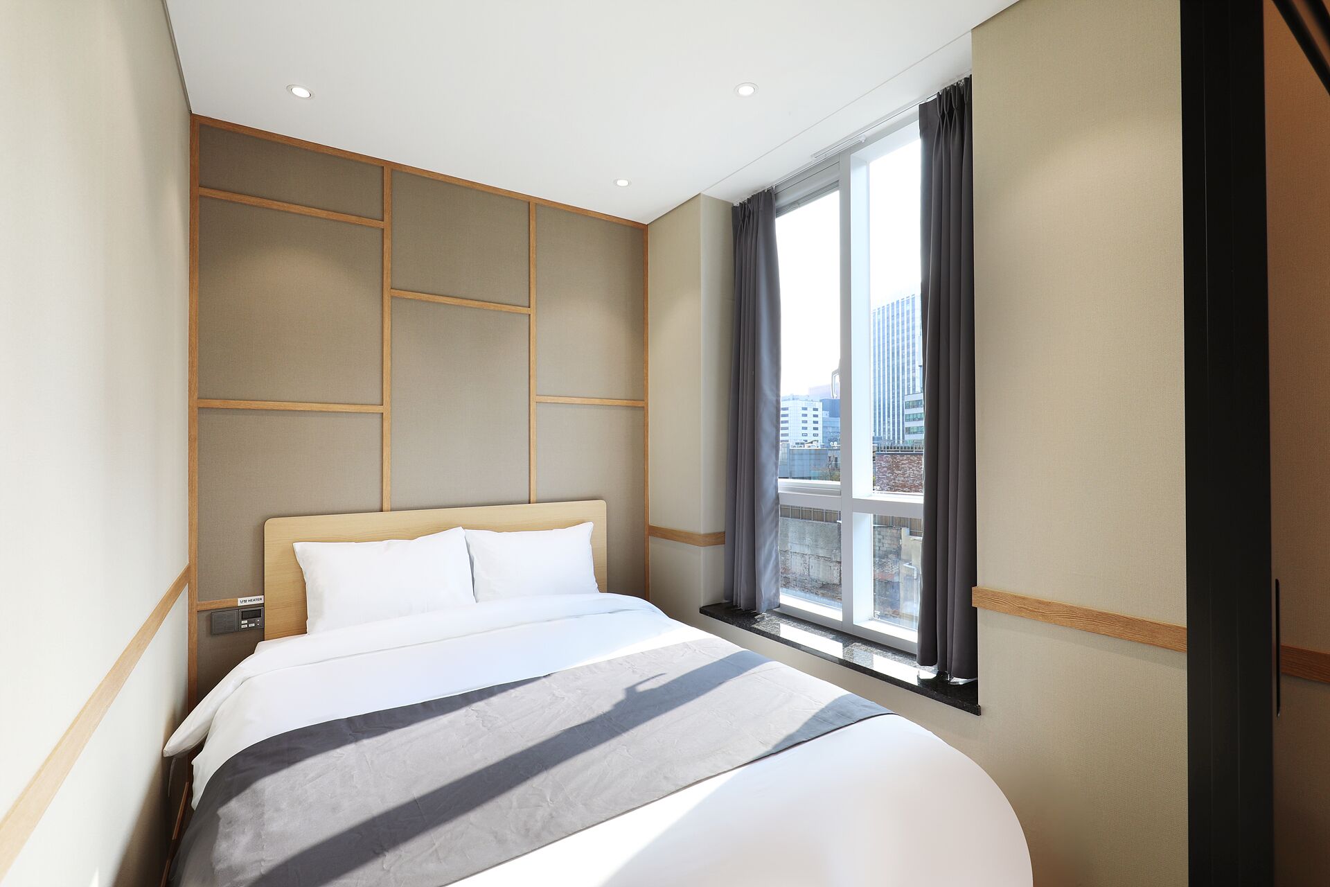 A hotel room with a large bed, a control panel, and a window with a city view.
