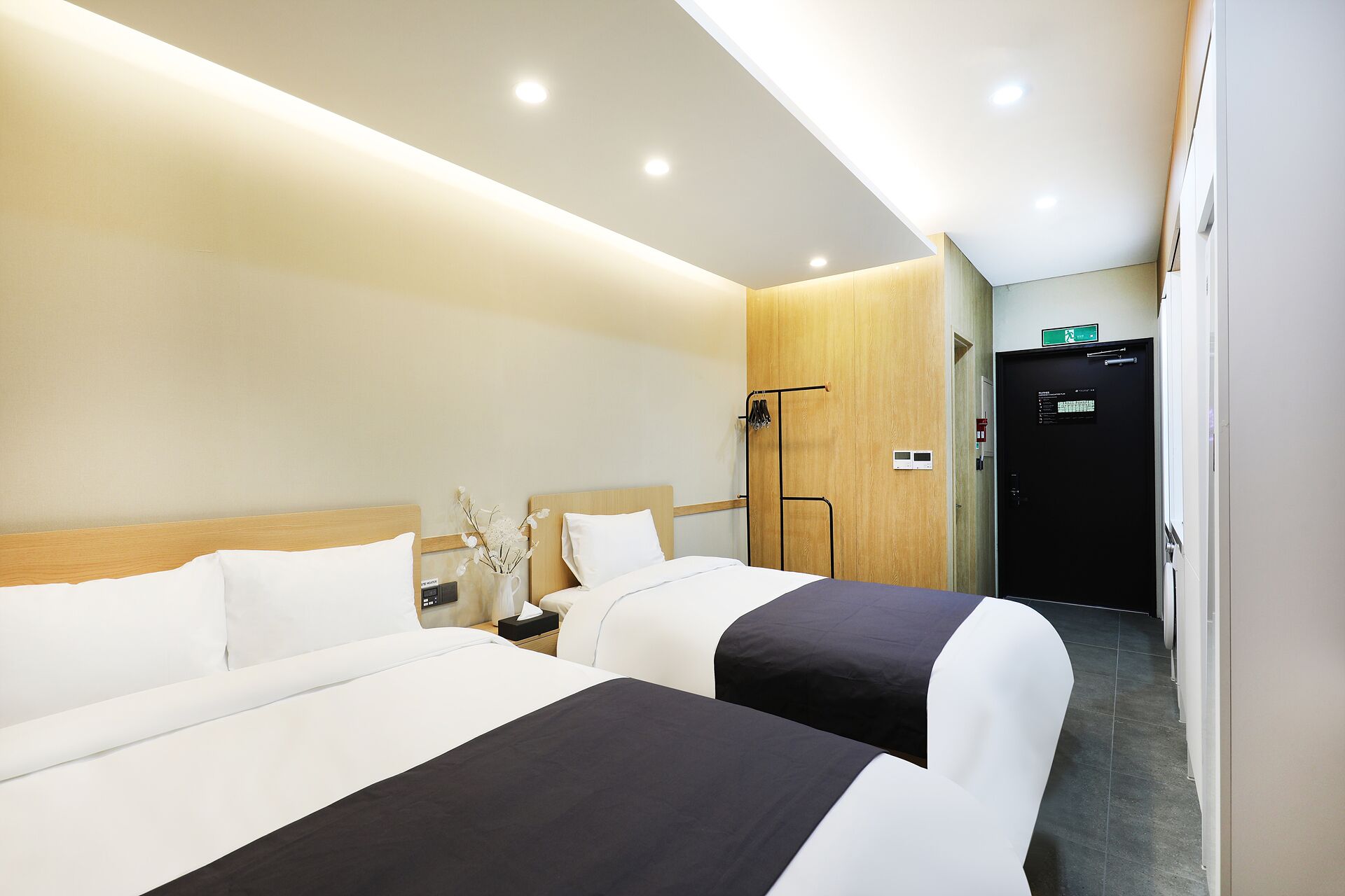 A hotel room with two beds, a wooden wardrobe, a nightstand, and a wall-mounted control panel.