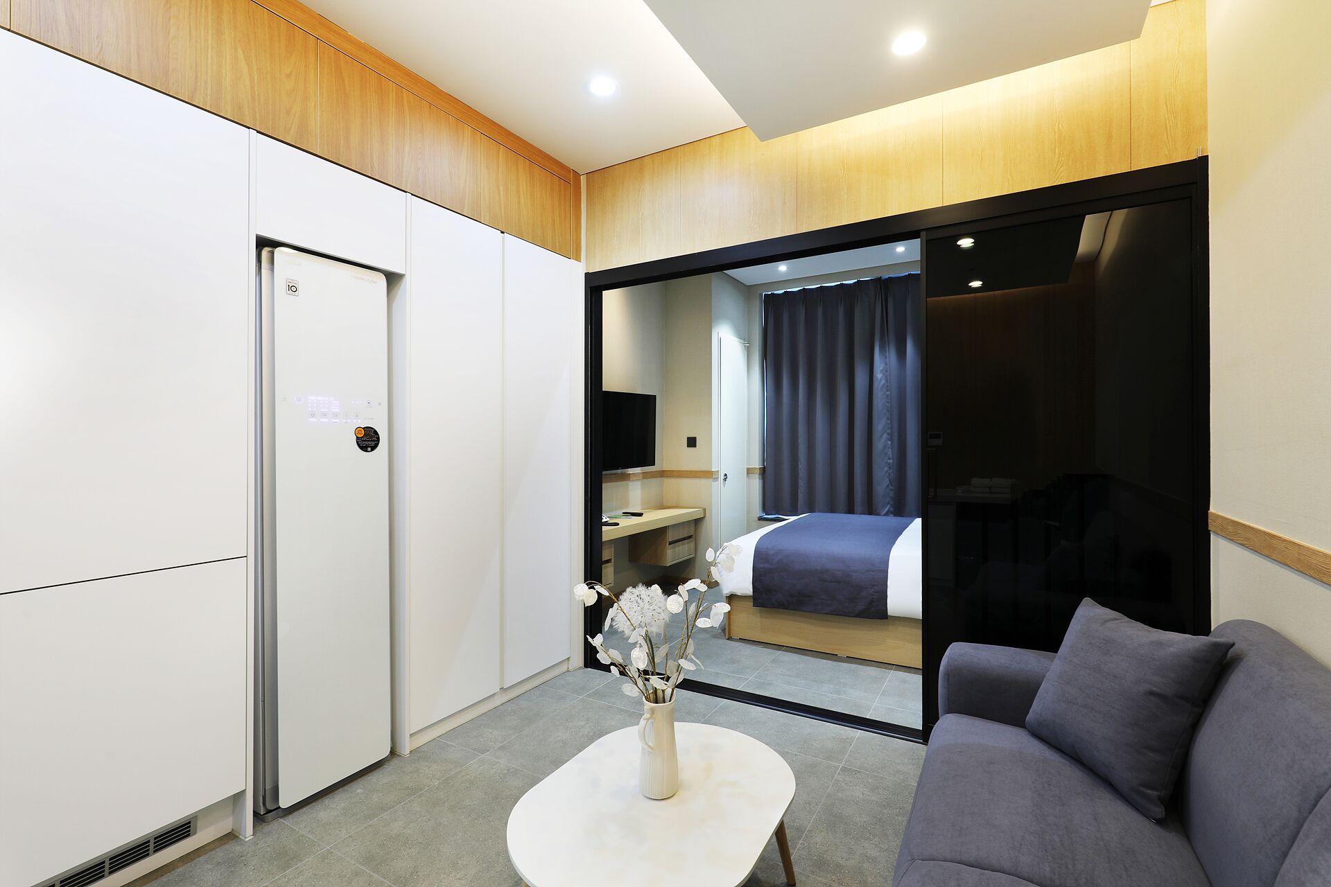 Una habitación de hotel moderna con una cama, un sofá, una mesita con un florero, un escritorio con una silla y un espejo grande.