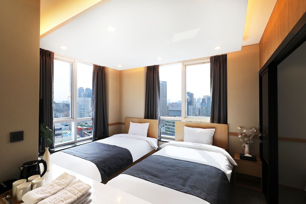 Hotelkamer met twee bedden, stadszicht, koffiezetapparaat en een vaas met bloemen.