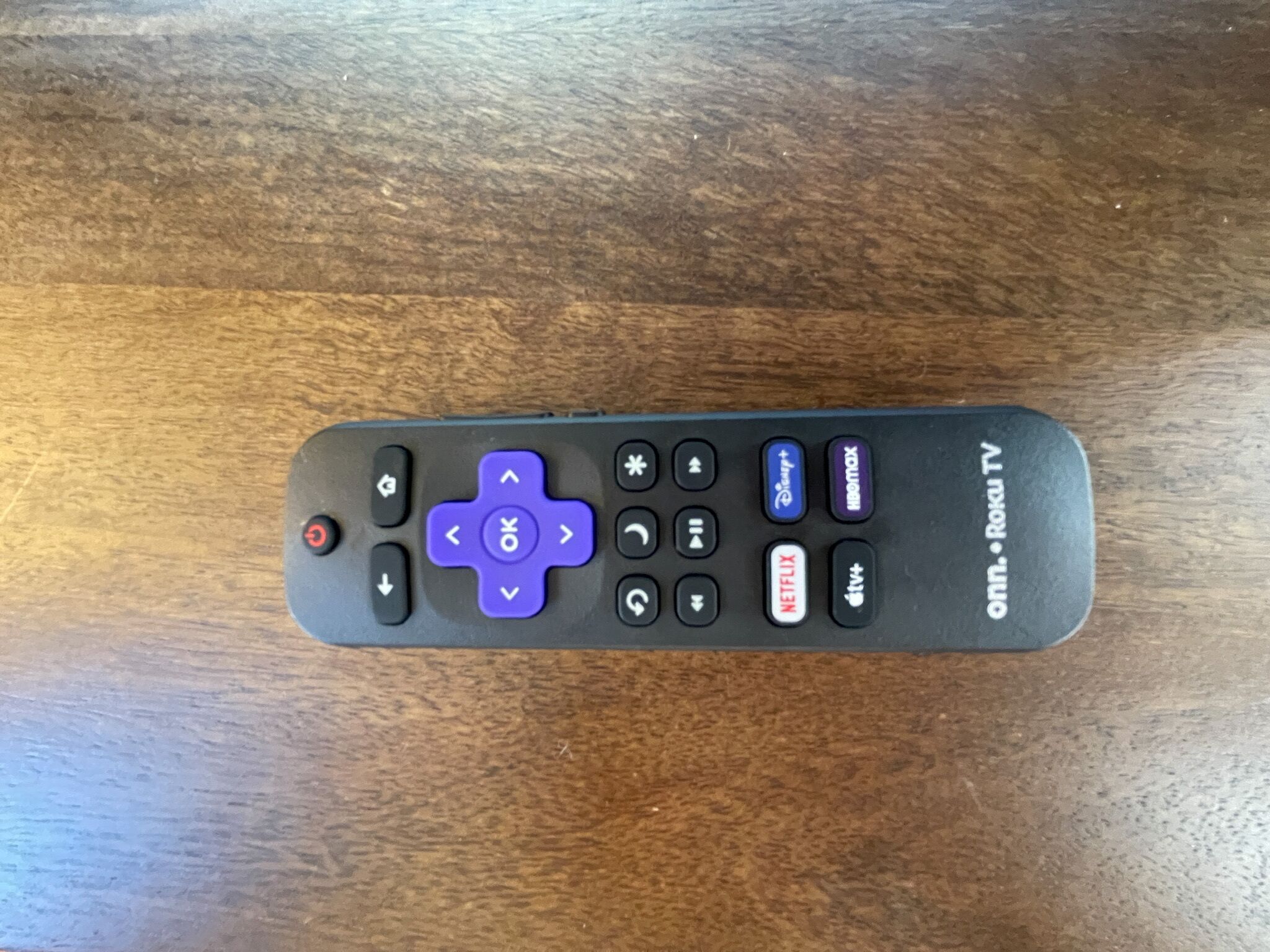 A remote control with directional pad, volume, and channel buttons, placed on a wooden surface.