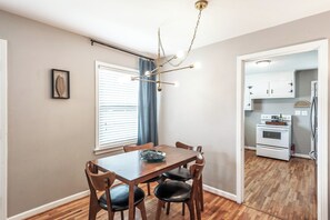 A dining area with a wooden table and chairs, a chandelier, and a view into the kitchen.