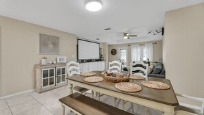 A dining area with a wooden table, white chairs, and woven placemats. - The Cozy Houz at Cimarron! With Golf Course View (Mission)