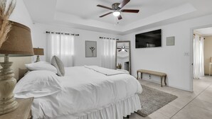 A bedroom with a bed, a ceiling fan, a bedside table with a lamp, a bench, and a large mirror. - The Cozy Houz at Cimarron! With Golf Course View (Mission)