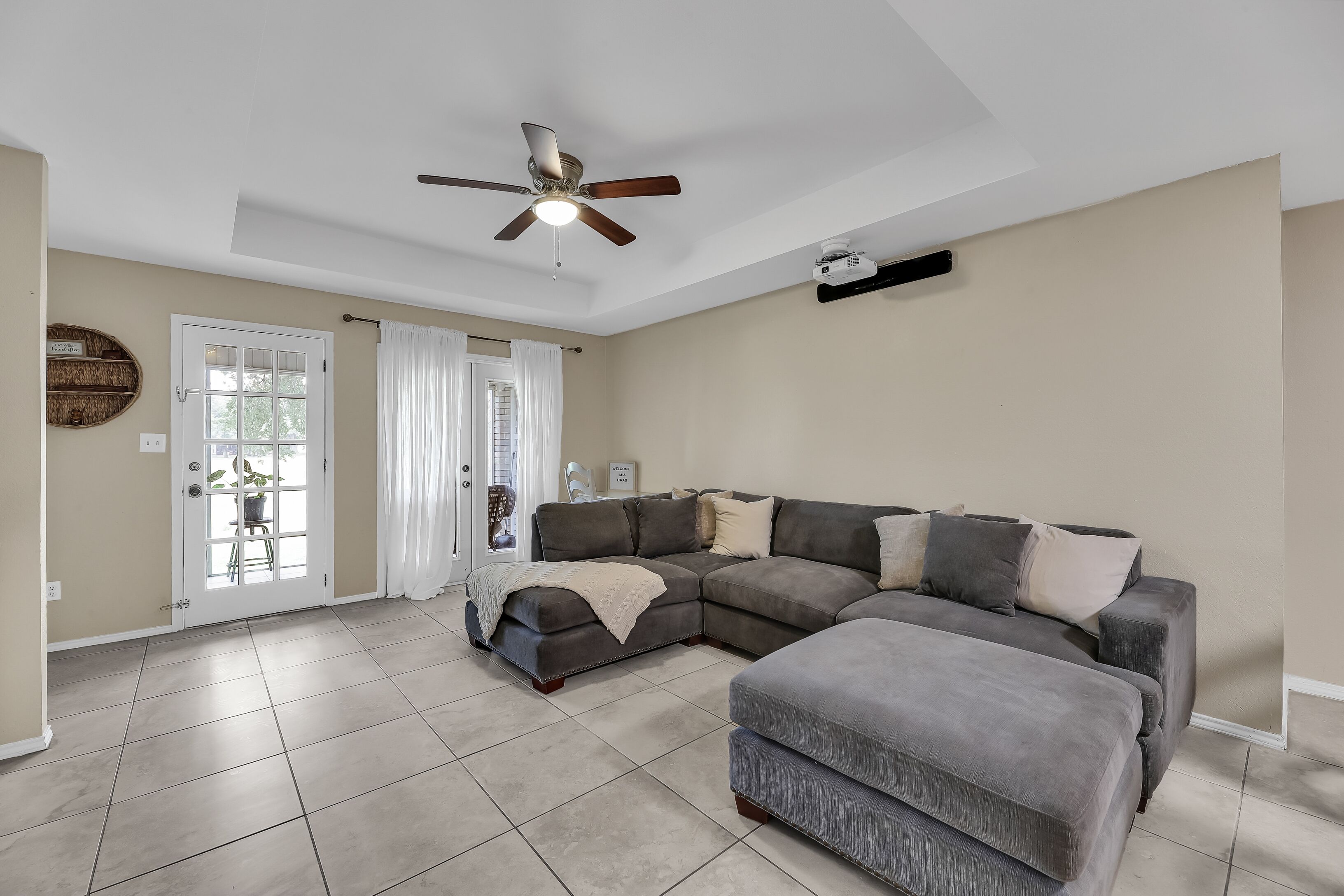 A living room with a sectional sofa, a ceiling fan, and a projector mounted on the wall.