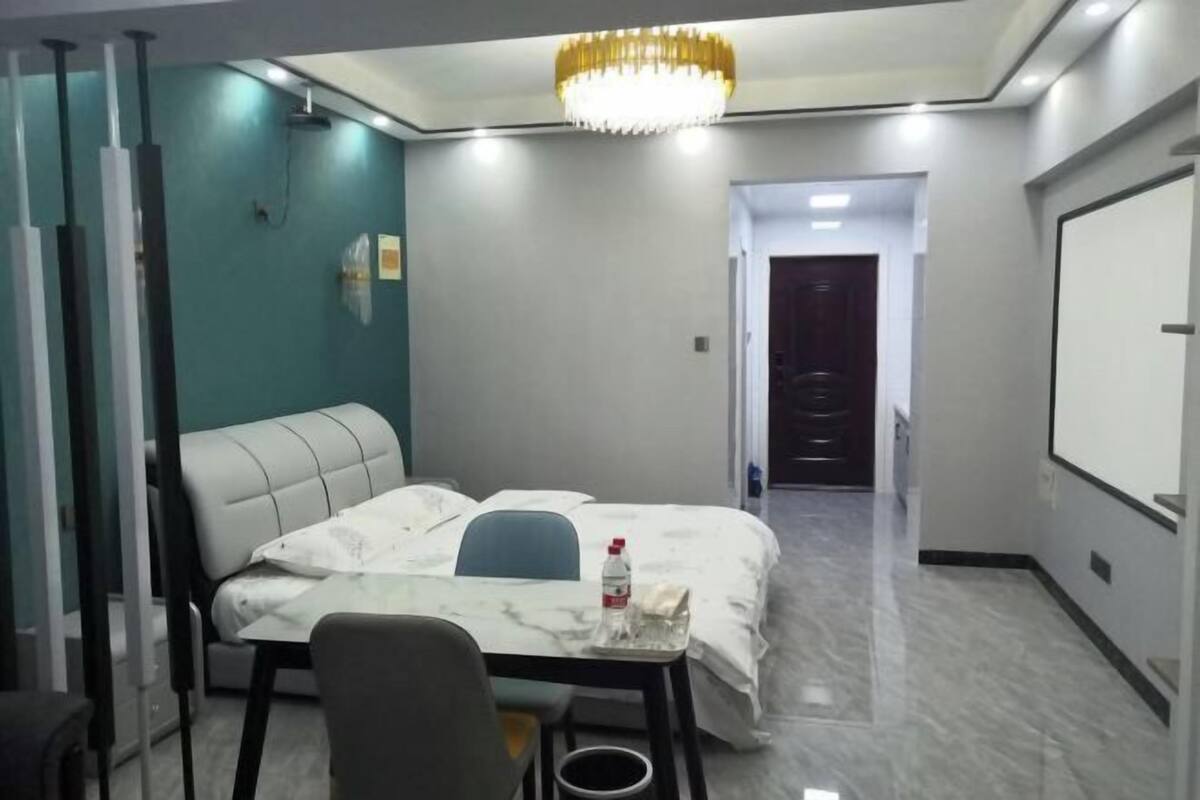 A hotel room with a bed, a desk, a chair, a chandelier, and a door leading to another room.