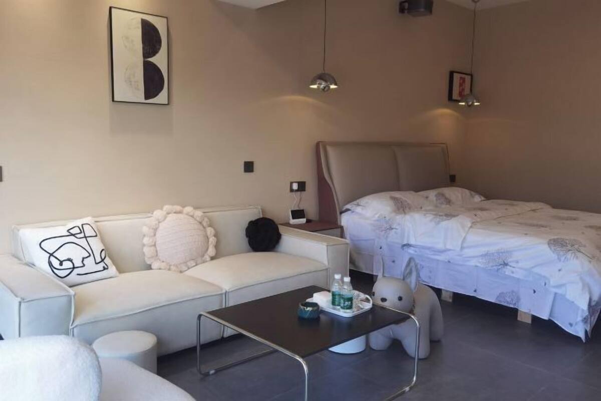 A modern hotel room with a bed, a sofa, a coffee table, and a wall-mounted artwork.