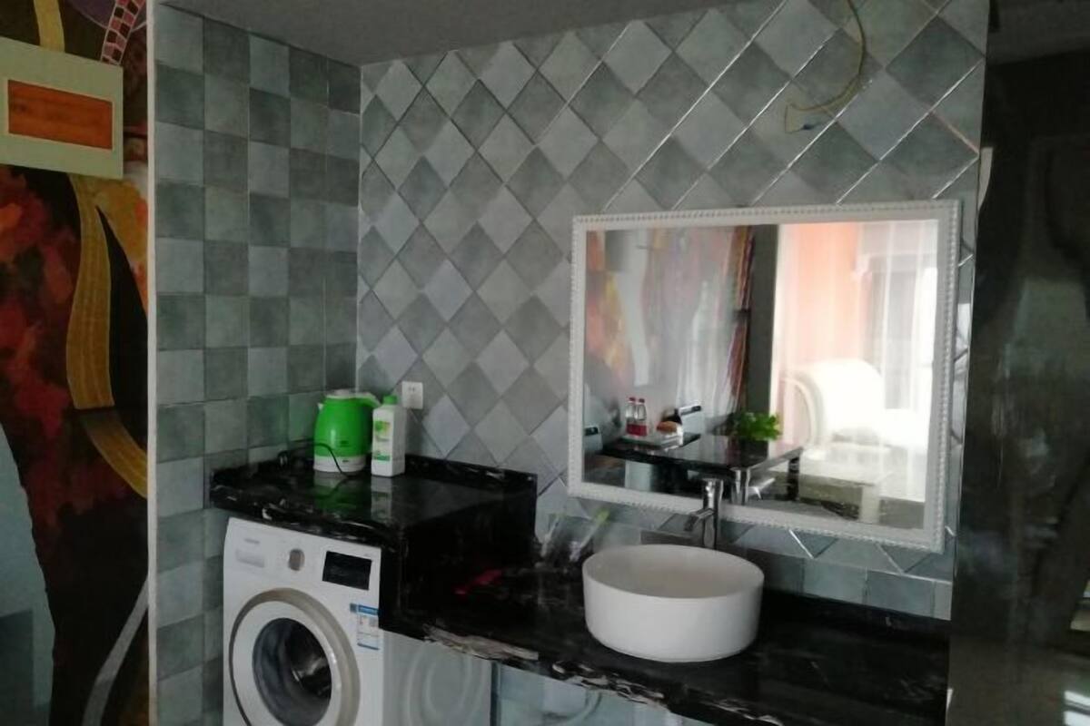 A compact bathroom with a washing machine, a sink, and a mirror.