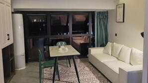 A compact living space with a white sofa, a dining table with chairs, and a large window with curtains. - Chuzhou Aidi Daily and Short-Term Rental Luxury Apartment (Chuzhou)