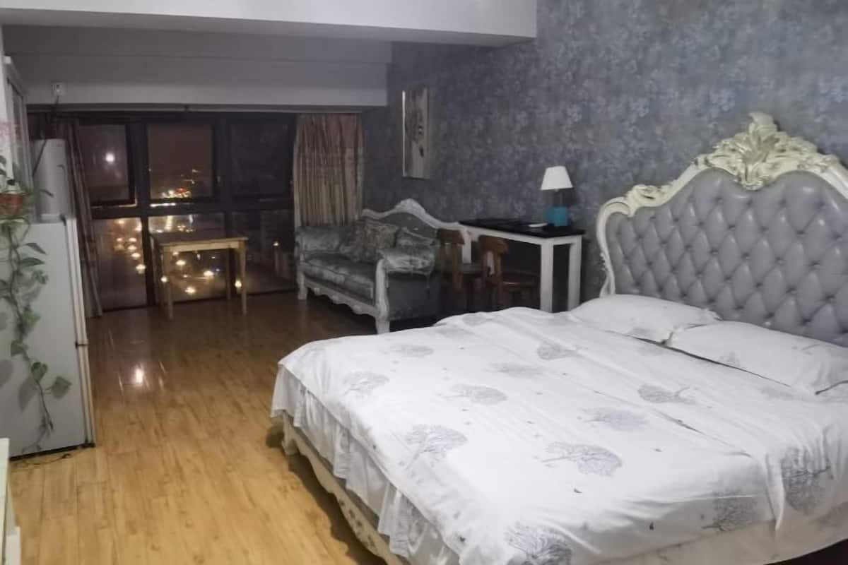 A bedroom with a bed, a small table with a lamp, a chair, and a view through a glass door to the outside.