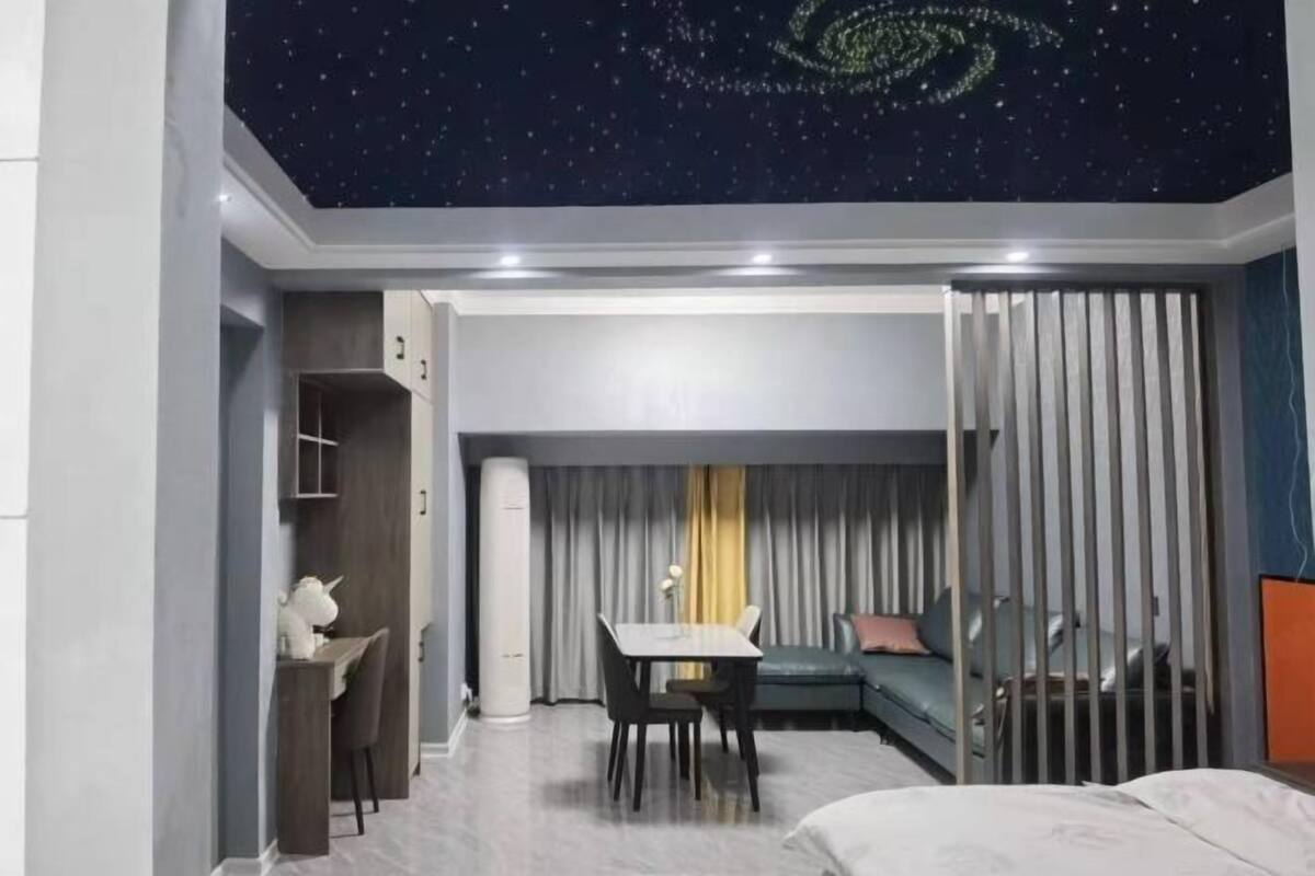 A hotel room with a starry ceiling, a dining area, a sofa, and a bed.